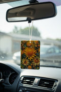 A rectangular car air freshener with a vibrant yellow and orange sunflower print hangs from a white string under a rearview mirror inside a car.