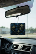 A rectangular car air freshener with a skull and blue rose pattern hanging from a rearview mirror inside a car.