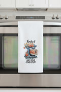 White towel with a decorative design and text on a black rod against a neutral wall.